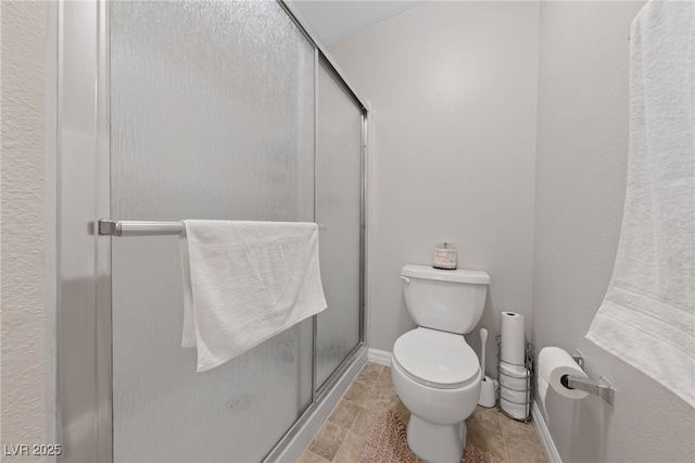 bathroom featuring baseboards, toilet, and a stall shower