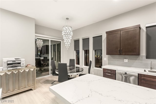 kitchen with stainless steel dishwasher, a sink, dark brown cabinets, a notable chandelier, and light stone countertops