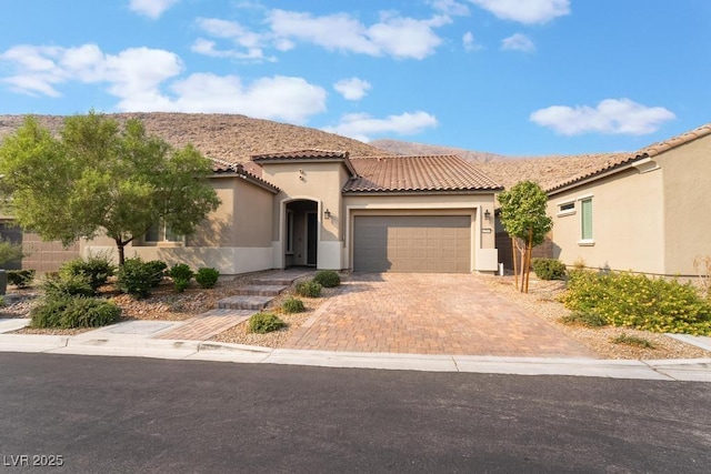 mediterranean / spanish-style home with an attached garage, a tile roof, driveway, and stucco siding