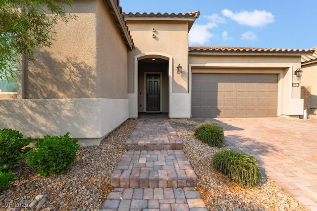 doorway to property featuring stucco siding, a tiled roof, decorative driveway, and a garage