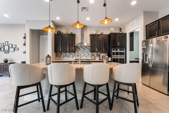 kitchen featuring wall chimney range hood, decorative light fixtures, backsplash, appliances with stainless steel finishes, and visible vents