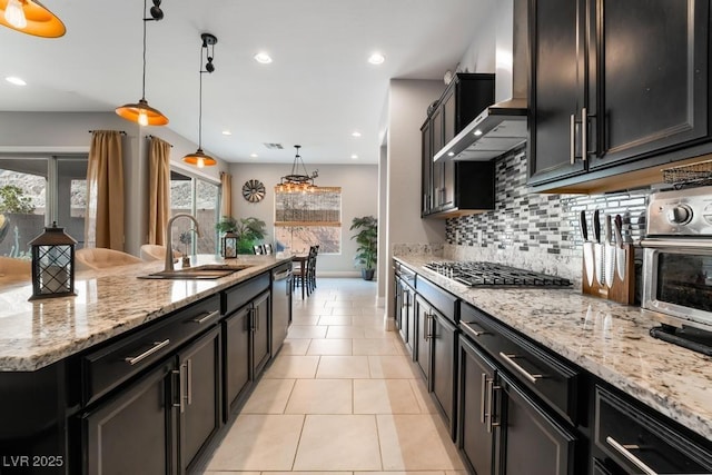 kitchen featuring dark cabinets, a sink, appliances with stainless steel finishes, and wall chimney range hood
