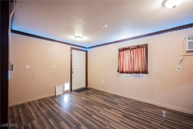 empty room with an AC wall unit, baseboards, and dark wood-style flooring