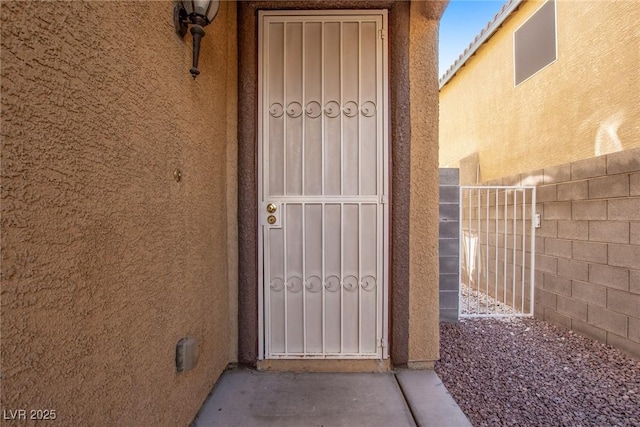 view of exterior entry with stucco siding and fence