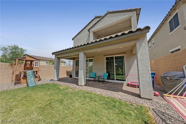 rear view of property with a tile roof, a fenced backyard, a playground, a patio, and stucco siding