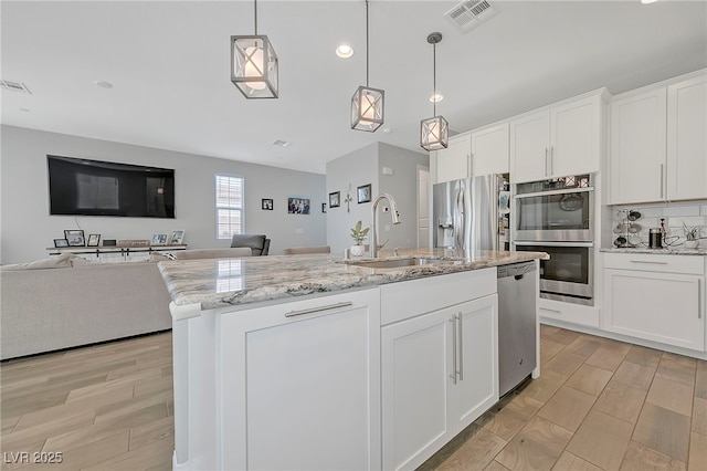 kitchen with stainless steel appliances, visible vents, a sink, a kitchen island with sink, and open floor plan