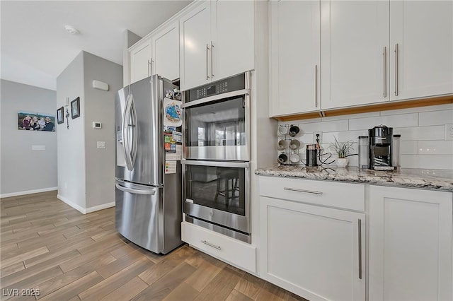 kitchen featuring light wood finished floors, light stone countertops, baseboards, appliances with stainless steel finishes, and white cabinetry