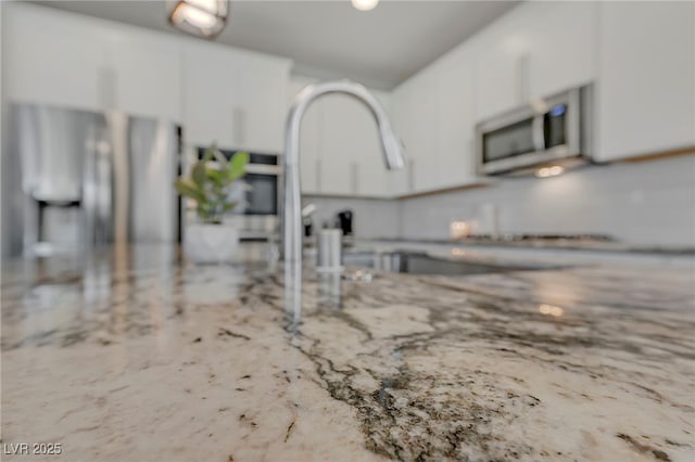 interior details with stainless steel microwave, light stone countertops, and white cabinetry