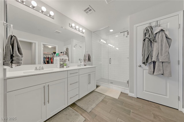 full bath featuring double vanity, visible vents, a sink, a walk in closet, and a stall shower