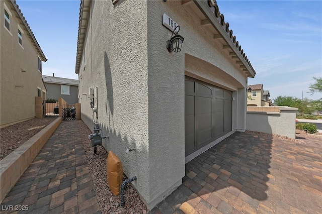 view of property exterior with a garage, driveway, stucco siding, and fence