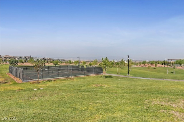 view of property's community with fence, a lawn, and a tennis court