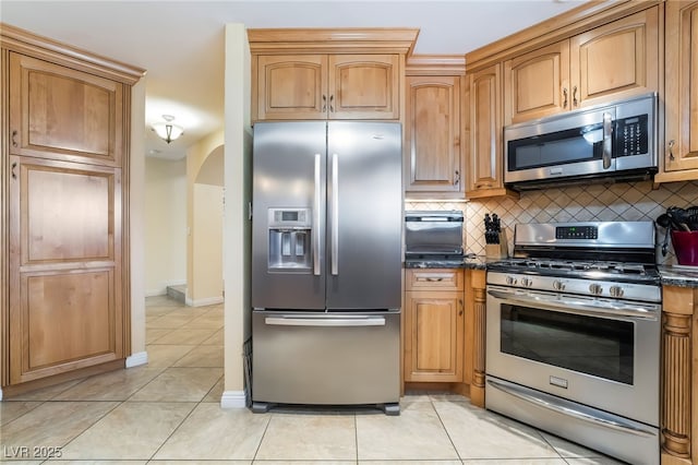 kitchen with appliances with stainless steel finishes, arched walkways, decorative backsplash, light tile patterned floors, and baseboards