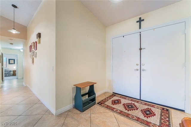 foyer entrance featuring lofted ceiling, light tile patterned floors, and baseboards