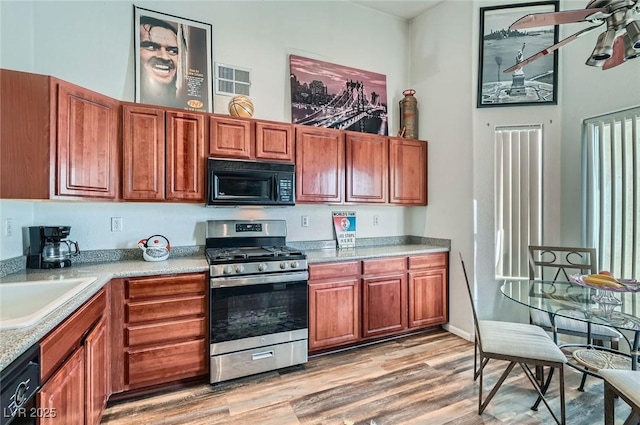 kitchen with light countertops, a sink, light wood-style floors, black appliances, and ceiling fan