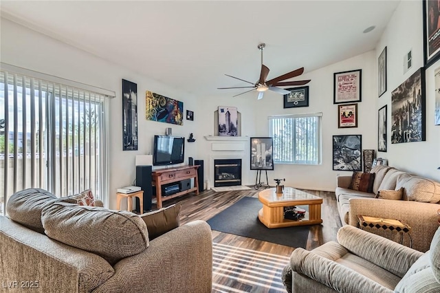 living area featuring a wealth of natural light, a ceiling fan, a glass covered fireplace, and wood finished floors