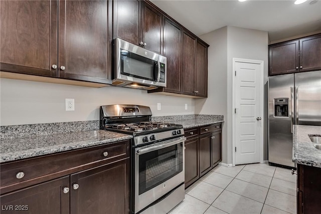 kitchen featuring light tile patterned flooring, dark brown cabinets, light stone countertops, and stainless steel appliances