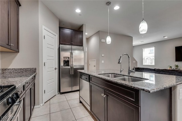 kitchen featuring stainless steel appliances, a kitchen island with sink, a sink, dark brown cabinetry, and light stone counters