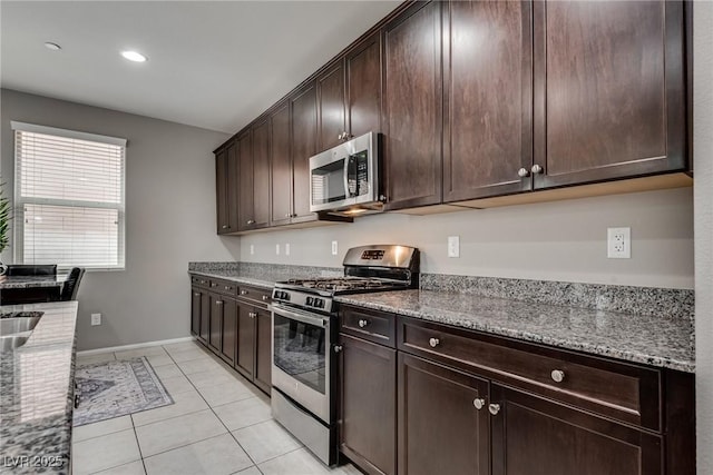 kitchen with light tile patterned floors, stainless steel appliances, dark brown cabinetry, and light stone counters