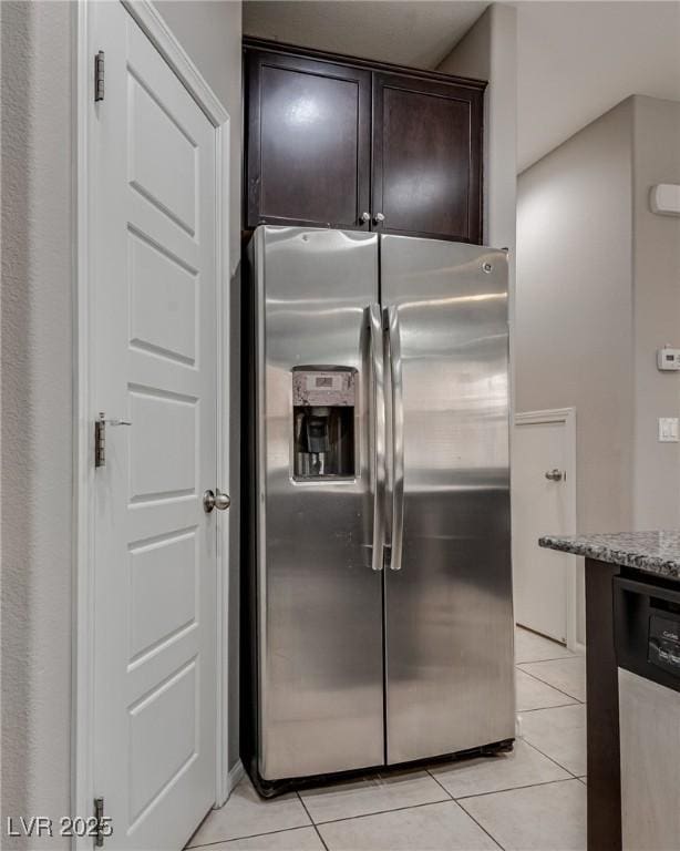kitchen with stainless steel fridge, dark brown cabinets, light stone counters, and light tile patterned floors
