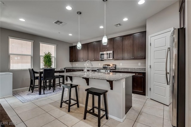 kitchen with light stone counters, dark brown cabinetry, stainless steel appliances, and visible vents