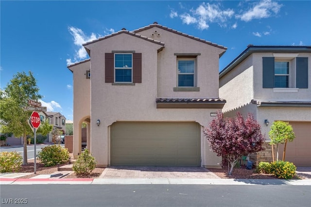 mediterranean / spanish home featuring a garage, a tile roof, stucco siding, and decorative driveway