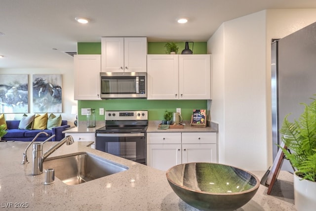 kitchen with white cabinets, light stone countertops, a sink, and appliances with stainless steel finishes