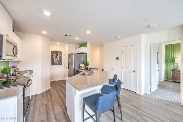 kitchen with a sink, a breakfast bar area, stainless steel appliances, light wood-style flooring, and white cabinets