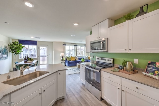 kitchen with light stone counters, a sink, light wood-type flooring, stainless steel appliances, and white cabinetry