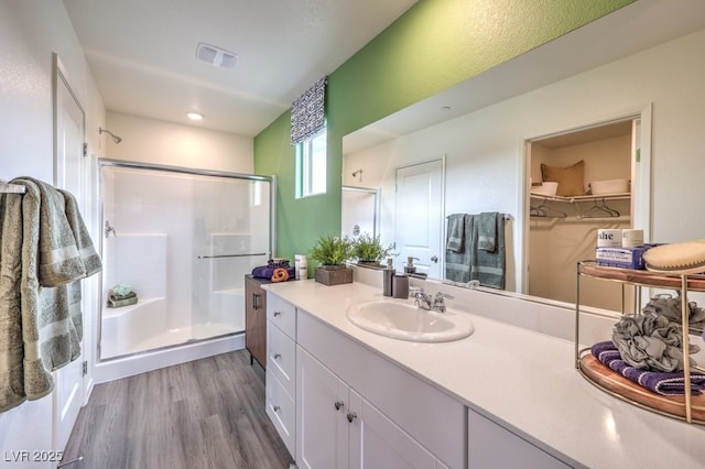 bathroom featuring visible vents, wood finished floors, a shower stall, vanity, and a walk in closet