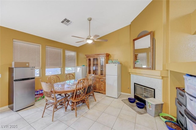 dining space featuring vaulted ceiling, a ceiling fan, light tile patterned floors, a premium fireplace, and visible vents