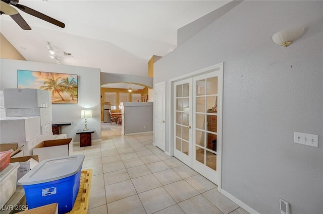 hall featuring french doors, arched walkways, vaulted ceiling, tile patterned flooring, and rail lighting