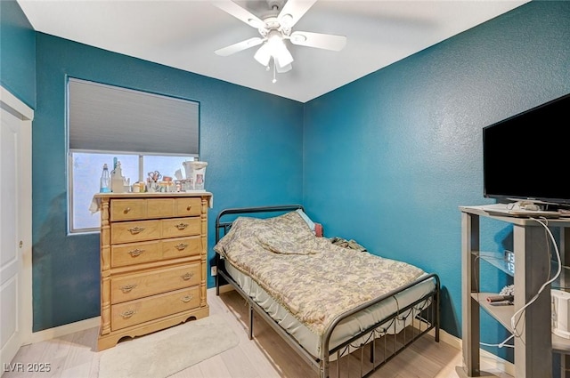 bedroom featuring baseboards, a ceiling fan, wood finished floors, and a textured wall
