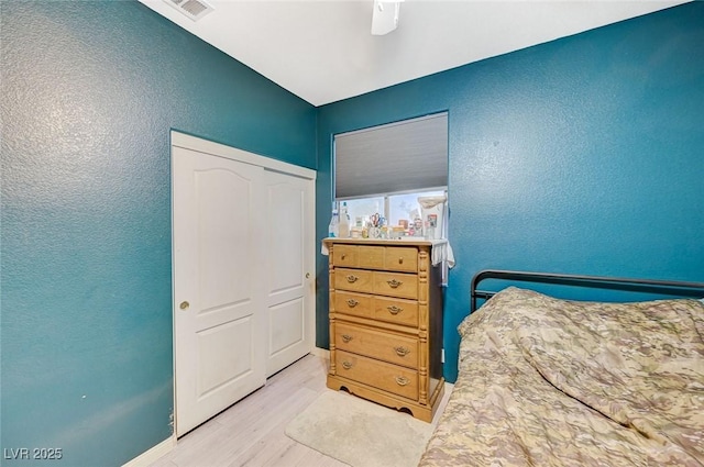 bedroom featuring a ceiling fan, a closet, a textured wall, light wood-style flooring, and baseboards