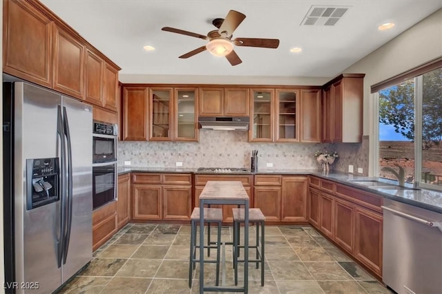 kitchen with brown cabinets, under cabinet range hood, visible vents, a sink, and appliances with stainless steel finishes