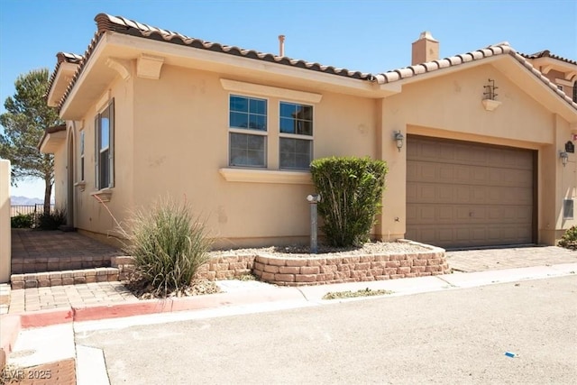 view of front of house featuring stucco siding, an attached garage, a chimney, and a tiled roof
