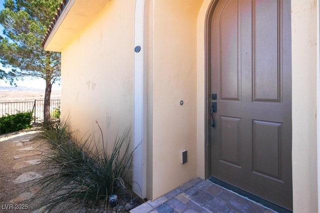 view of exterior entry with stucco siding and fence