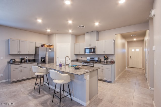 kitchen featuring an island with sink, a breakfast bar, baseboards, appliances with stainless steel finishes, and visible vents