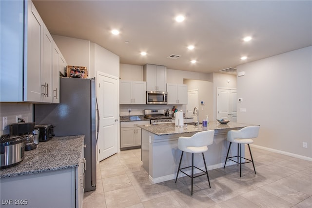 kitchen featuring a kitchen bar, stainless steel appliances, visible vents, and light tile patterned floors