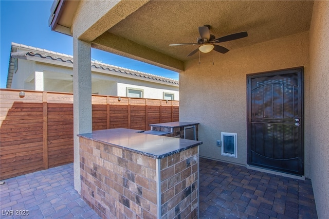view of patio featuring fence, ceiling fan, an outdoor kitchen, and exterior bar