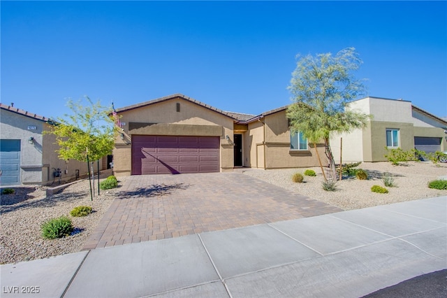 ranch-style home featuring an attached garage, a tile roof, decorative driveway, and stucco siding