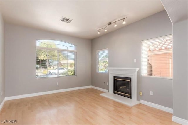 unfurnished living room featuring a glass covered fireplace, baseboards, visible vents, and light wood-style floors