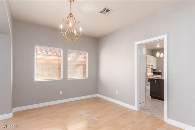 unfurnished room featuring baseboards, visible vents, light wood-style floors, and a notable chandelier
