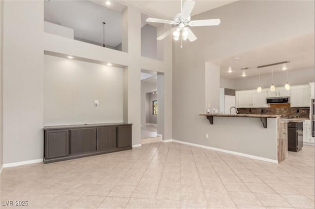 unfurnished living room featuring a high ceiling, a ceiling fan, baseboards, and light tile patterned floors