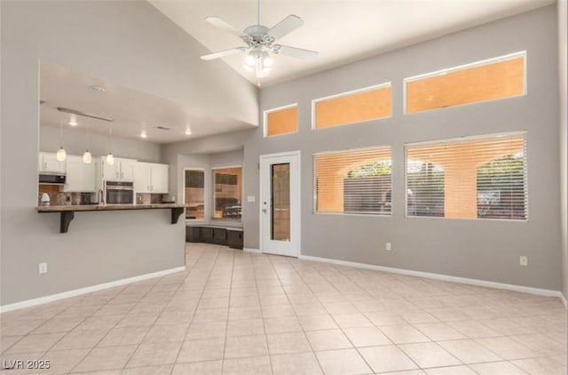unfurnished living room featuring a high ceiling, baseboards, ceiling fan, and light tile patterned floors