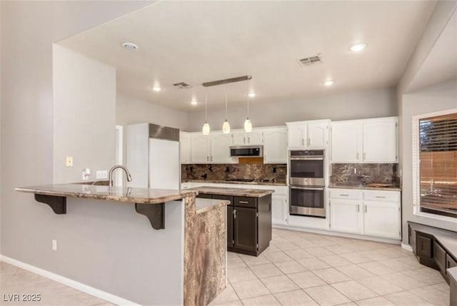 kitchen with light stone counters, backsplash, visible vents, a kitchen bar, and appliances with stainless steel finishes