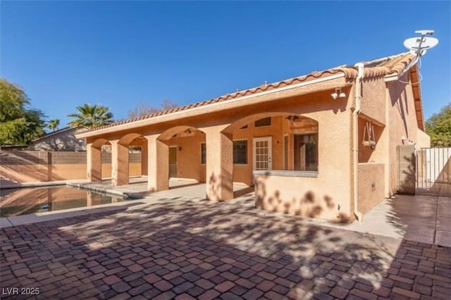rear view of property with fence, a patio area, a tile roof, and stucco siding