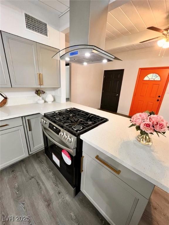 kitchen featuring stainless steel range with gas cooktop, island exhaust hood, dark wood-style floors, visible vents, and gray cabinets