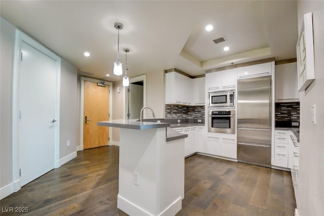 kitchen with decorative backsplash, dark wood-style flooring, white cabinets, a peninsula, and built in appliances