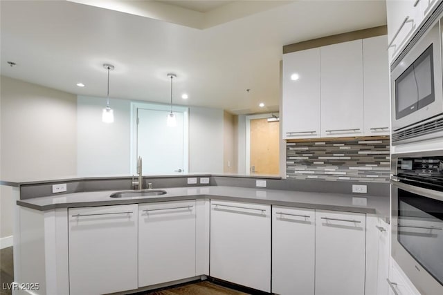kitchen with a sink, a peninsula, stainless steel appliances, recessed lighting, and white cabinetry