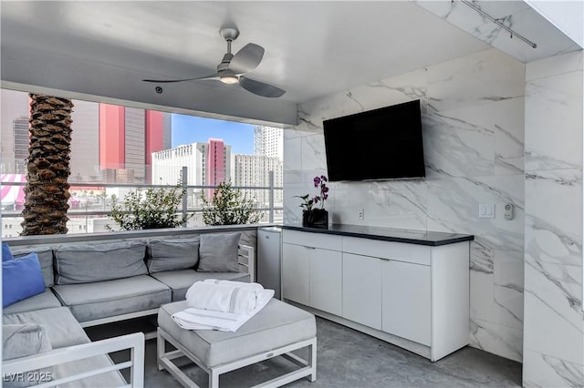 living area featuring tile walls, a ceiling fan, and concrete floors